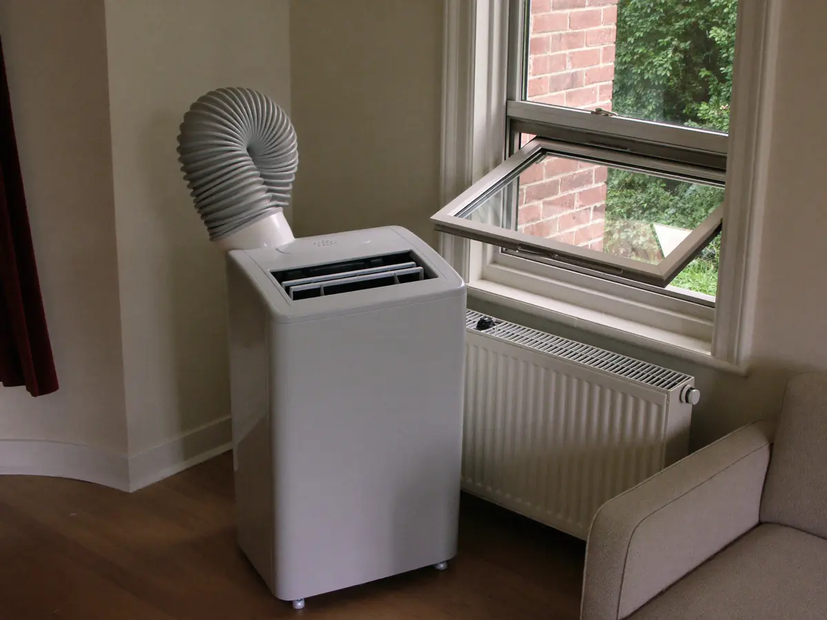 Mobiele airco met een afvoerslang naar een open raam in een kamer